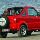 A red Suzuki Jimny parked by a beach